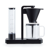 A PERFORMANCE BLACK coffee maker with a transparent water reservoir and a glass carafe filled with coffee. Featuring unique technology for the perfect temperature, it boasts two award badges: one with a laurel wreath indicating "Best i Test Tek.no" and another that reads "Testvinner" with stars and a ribbon symbol.