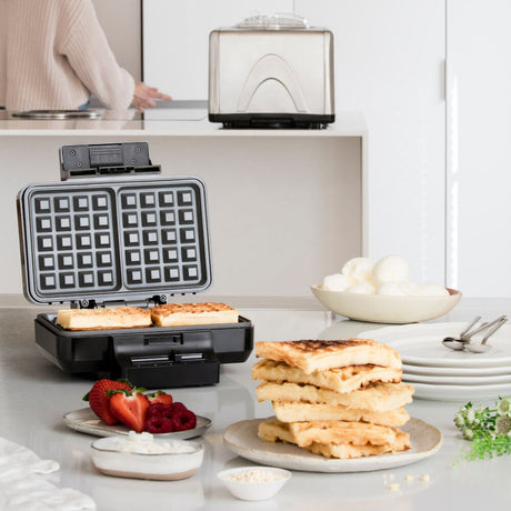 A sleek black GAUFRES BELGIAN with silver accents is pictured against a white background. A gold and black badge with the text "TESTVINNER" is displayed in the top left corner, indicating it has been awarded a test winner. The waffle maker features adjustable temperature and double release coating for perfect waffles every time.